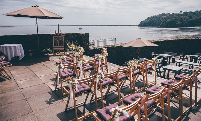 Wooden chairs with purple cushions set out on the Boathouse patio with a sunny Taf estuary in the background